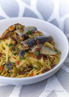 a white bowl filled with pasta and fish on top of a table next to a napkin