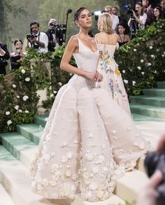 a model walks down the runway in a white gown with flowers on it and people taking pictures