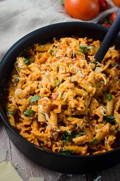 a skillet filled with pasta and vegetables on top of a wooden table next to tomatoes