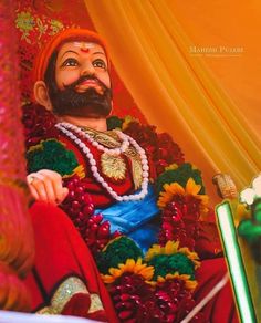 a man with a beard wearing a red outfit and beads sitting in front of a curtain