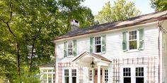 a large white house with green shutters on the front and side windows, surrounded by trees