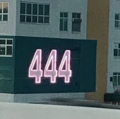 a neon sign that reads 444 on the side of a building in front of some buildings