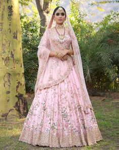 a woman in a pink lehenga standing next to a tree