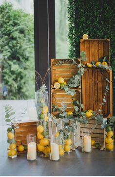 an arrangement of lemons and greenery is displayed in front of a window with candles