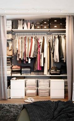 an organized closet with clothes hanging on the rails and drawers in front of it, next to a bed