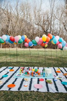 a table topped with lots of balloons and confetti on top of a black and white blanket