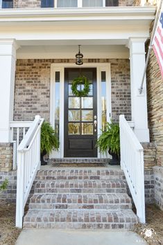 a front porch with steps leading up to the door and wreath on the side of the house