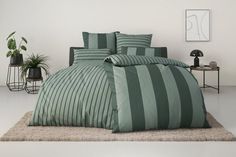 a bed with green and grey striped comforter in a room next to potted plants