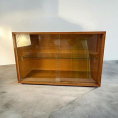 a wooden display case with glass shelves on the top and bottom shelf, in front of a white wall