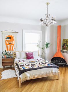 a bedroom with white walls and wooden floors, an orange fireplace in the corner, and a quilt on the bed