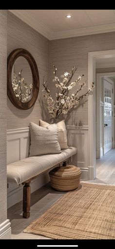 a white bench sitting next to a wooden table in a living room under a mirror