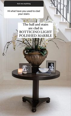 a table with flowers and pictures on it in front of a stair case that says, the hall and stairs are both potting light polished marble