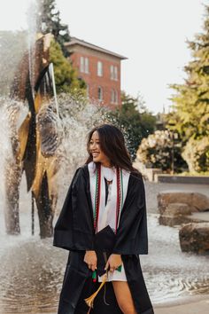 a woman in a graduation gown is walking by an elephant fountain