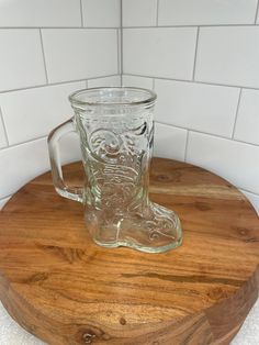 a clear glass mug sitting on top of a wooden table next to a white tile wall