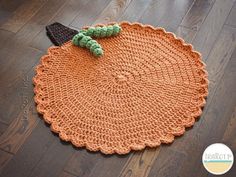 an orange crocheted placemat with a green leaf on it and a black hat