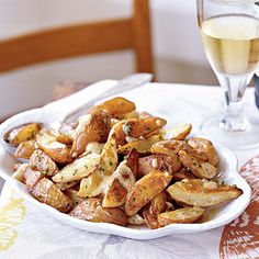 a white plate topped with potatoes next to a glass of wine