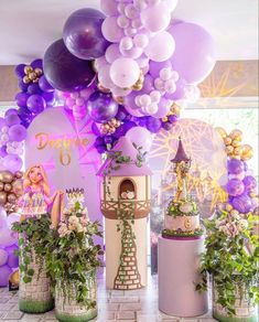 there are many balloons and plants on the table in front of the cake stand at this princess themed birthday party