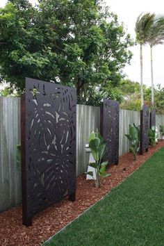 a fence that is next to some plants in the grass and trees on the other side