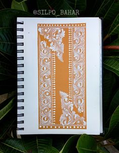 an orange and white patterned notebook sitting on top of green leaves