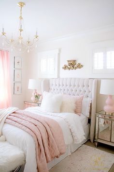 a white and pink bedroom with a chandelier, bed, nightstands, and rug