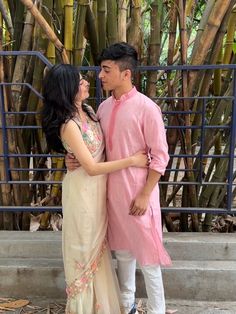 a man and woman standing next to each other in front of some bamboo trees with their arms around each other