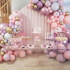 a table topped with lots of pink and gold balloons next to a wall filled with desserts