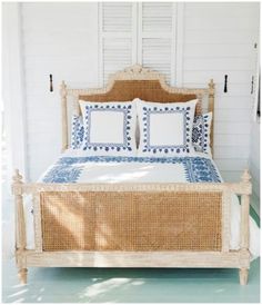 a wicker bed with blue and white pillows on the headboard is in front of a window