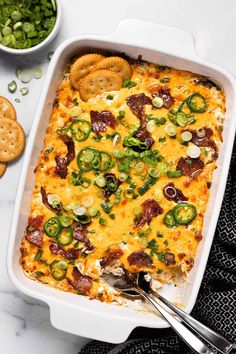 a white casserole dish filled with green onions, cheese and jalapenos