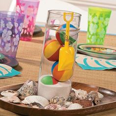 an assortment of beach balls in a glass vase on a table with plates and cups