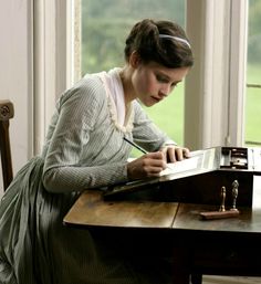 a woman sitting at a desk writing on a piece of paper in front of a window