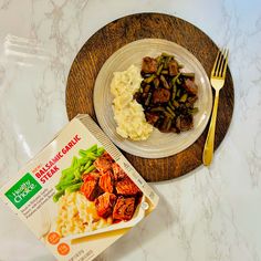 a plate with meat, mashed potatoes and green beans next to a packet of organic foods