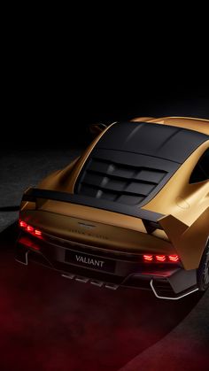 the rear end of a gold sports car with its lights on in a dark room