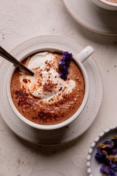 there is a cup of hot chocolate with whipped cream on top and purple flowers in the middle