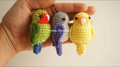 three small crocheted birds sitting on top of each other's fingers in front of a white wall