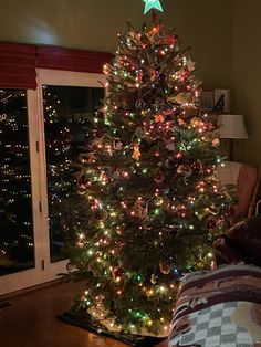 a lit christmas tree in the corner of a living room next to a couch and window