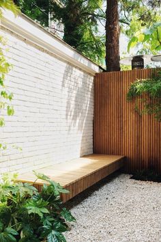 a wooden bench sitting next to a white brick wall and green trees in the background