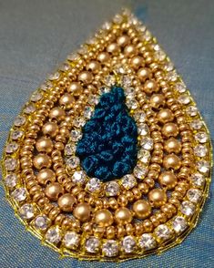 a blue and gold brooch sitting on top of a piece of cloth covered in beads