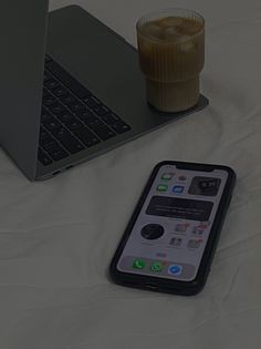 an open laptop computer sitting on top of a white bed next to a cell phone