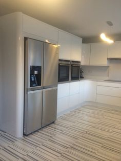 an empty kitchen with white cabinets and stainless steel refrigerator freezer combo in the middle