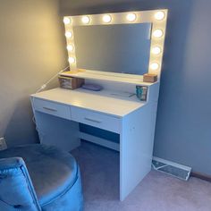 a white vanity with lights on it and a blue chair in front of the mirror