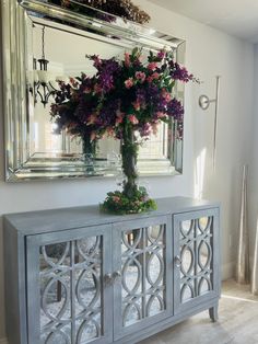 a vase filled with flowers sitting on top of a wooden cabinet next to a mirror