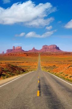 an empty road in the desert with mountains in the backgrouds and blue sky