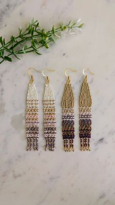 three pairs of beaded fringe earrings sitting on top of a marble table next to a plant