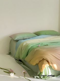 a bed with green and yellow sheets in a white room next to a flower on the floor