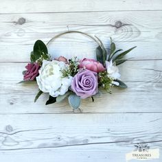 a wreath with flowers and greenery hanging on a white wooden wall in the shape of a circle