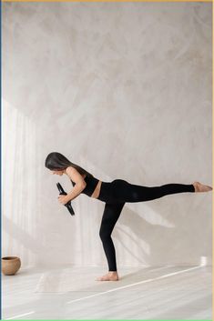 a woman in black is doing a yoga pose with her leg up and one foot on the ground