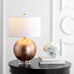 a table with a lamp and flowers on it next to a book, magazines and a vase