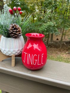 two red vases with pine cones are sitting on a porch railing, one has the word'single'painted on it