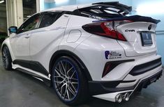 the rear end of a white car with blue rims and chrome wheels in a garage