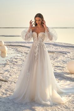 a woman in a wedding dress standing on the beach with her hands behind her head